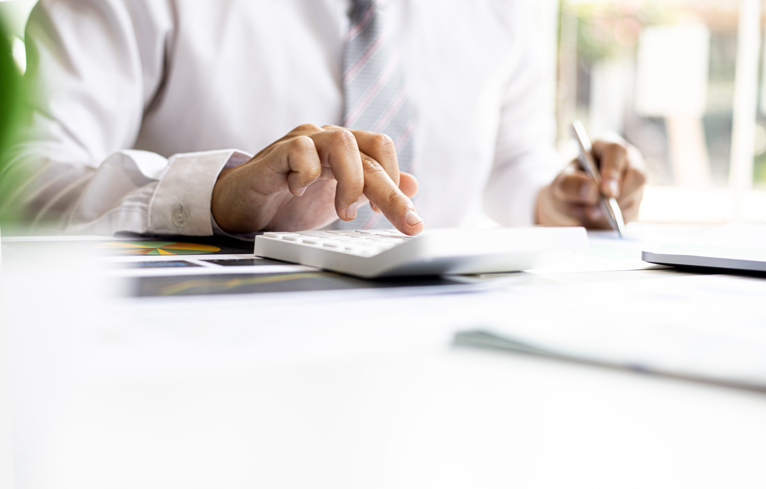 a business man is using a calculator to calculate company financial figures from earnings papers, a businessman sitting in his office where the company financial chart is placed. financial concept.