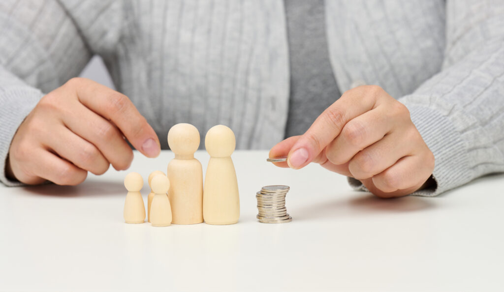 female hand puts coins in a pile and wooden figurines of a family on a white table. economy and investment concept, budget planning. receiving subsidies from the state, tax